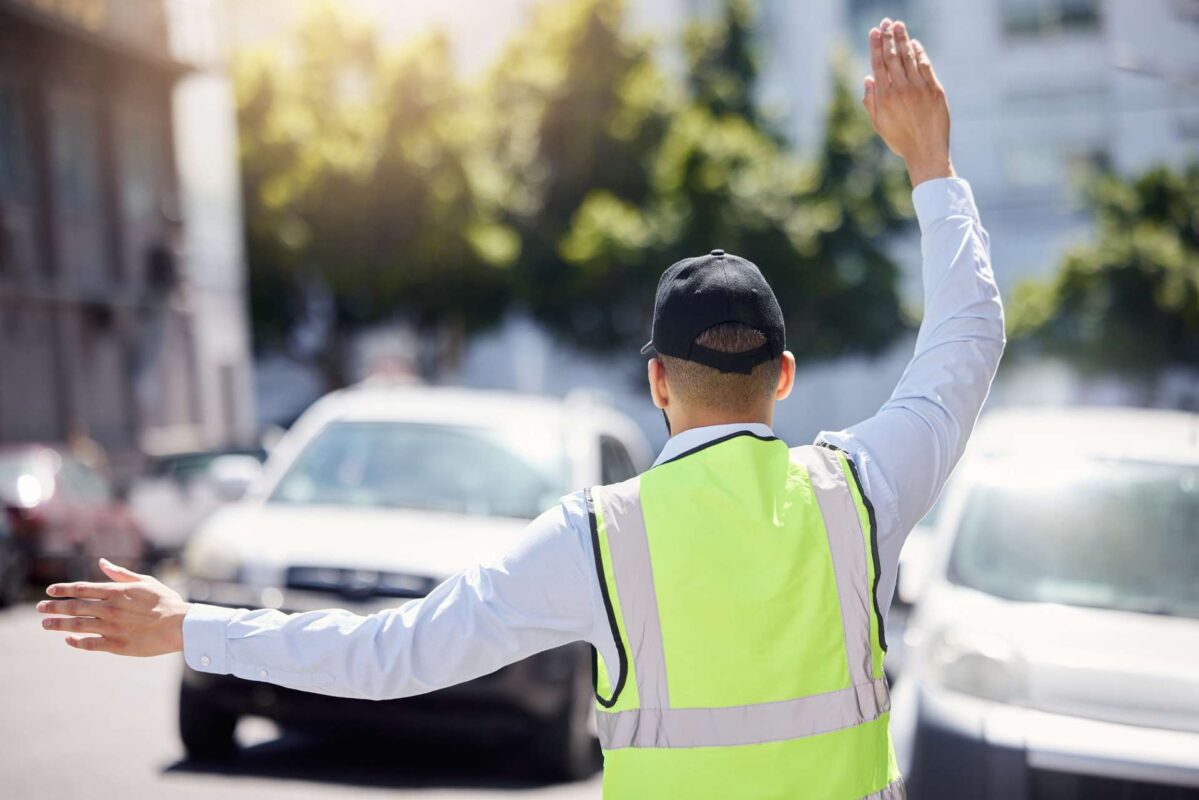 02 Man directing and controlling the flow of traffic rearview shot of traffic warden guiding vehicles outdoor_Encobridge FDOT TTC MOT Certification (Training)